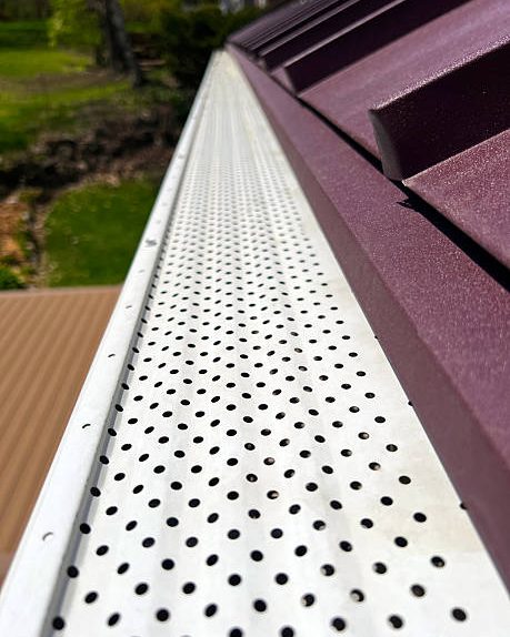A perforated metal gutter guard fitted over a gutter along the edge of a roof.