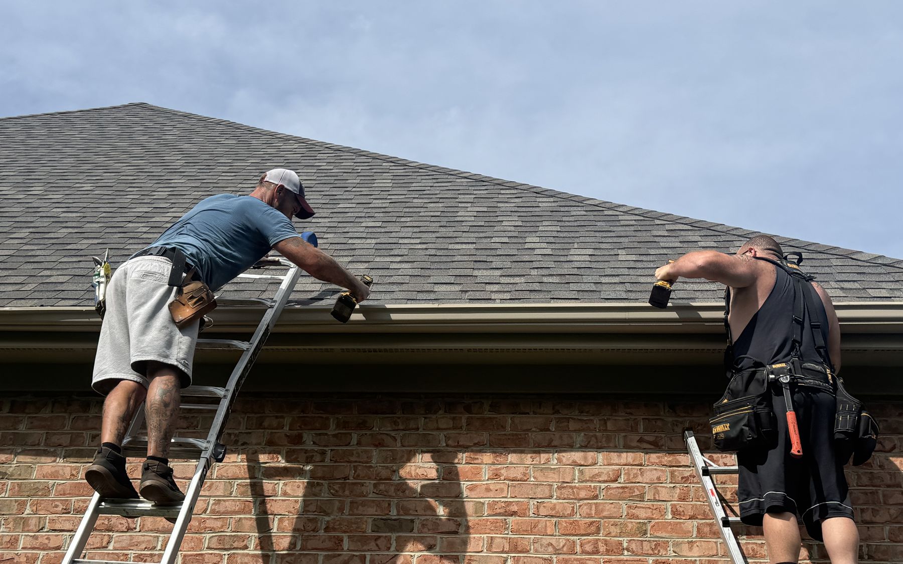 Two Elite Gutters installers working at the roofline of a brick home, fitting a new run of seamless gutter.