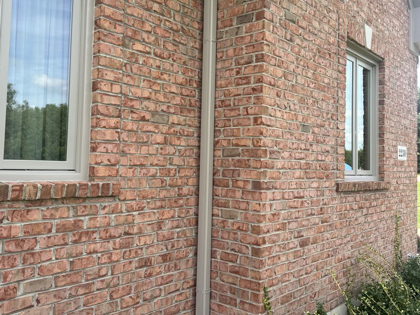 A finished downspout running down the brick corner of a home onto the stone below.