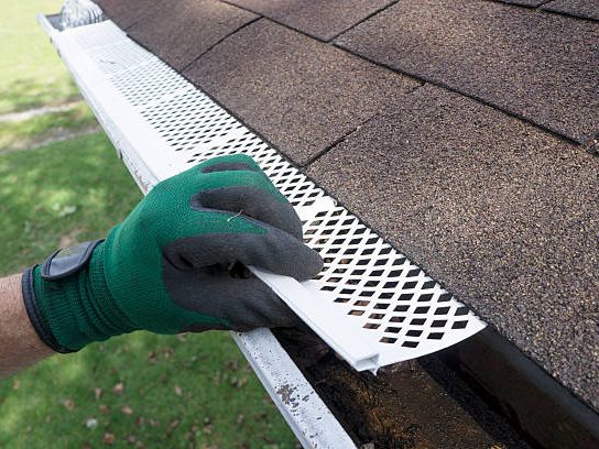 An installer fitting a perforated metal gutter guard over an open gutter.