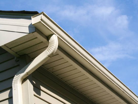 A newly installed white seamless gutter running along a roofline against a clear sky.