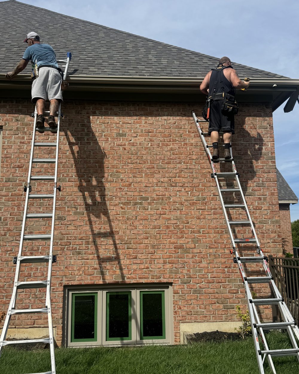 Two Elite Gutters installers on ladders fitting a run of seamless gutter along a two storey brick home.