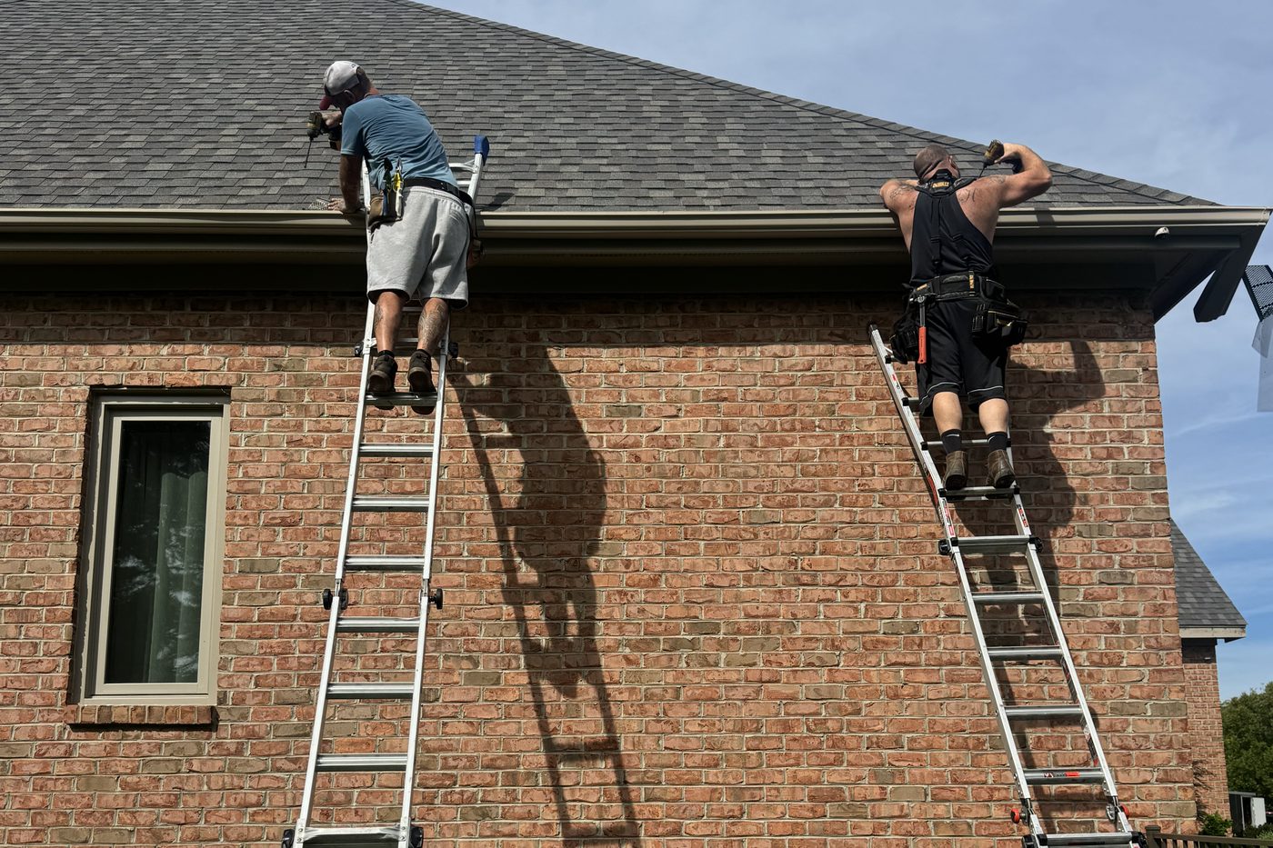 An Elite Gutters crew working from ladders along the side of a two storey brick home in the Dayton area.
